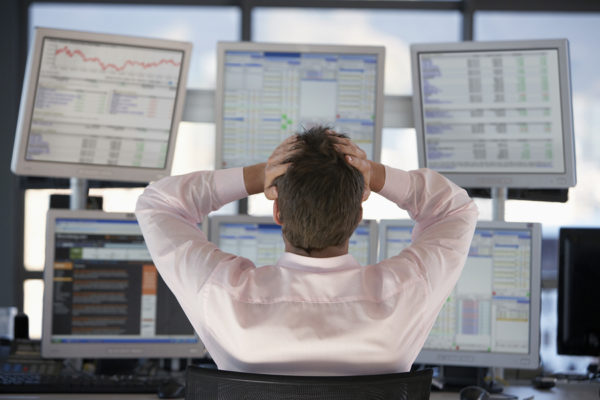 Rear view of stock trader with hands on head looking at multiple