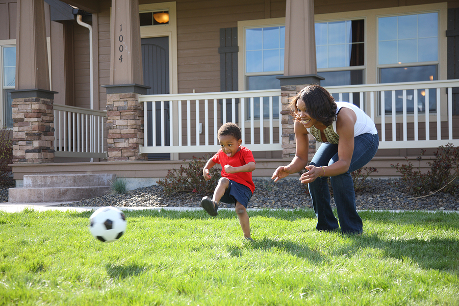 Mother and son in front yard playing with soccer ball